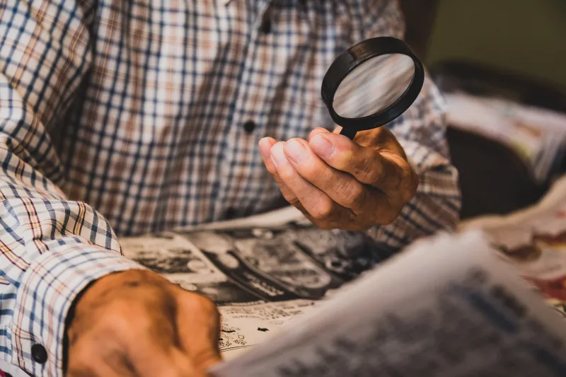 虫眼鏡で新聞を読む高齢者